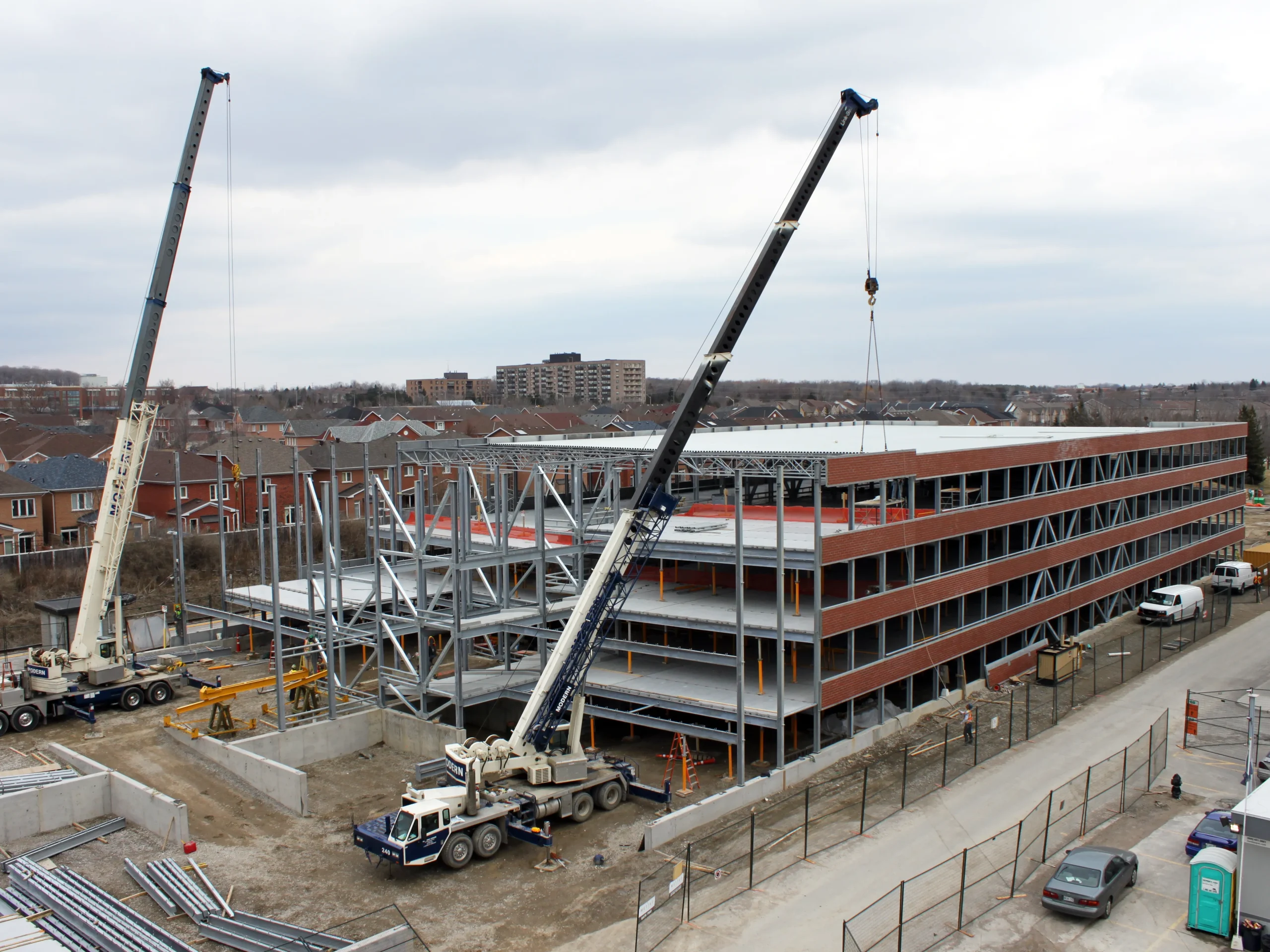 Multi-storey parking structure under construction with exposed framing and two mobile cranes.