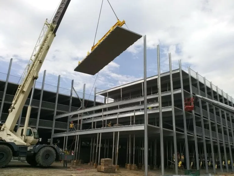Long grey prefabricated deck panel suspended by crane over garage structure