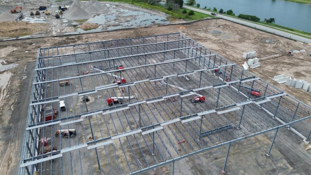 Drone view of rectangular industrial building frame with workers and lifts between bays