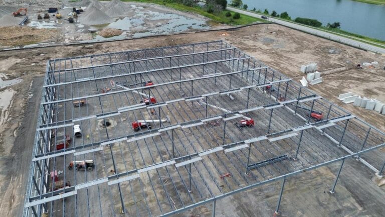 Drone view of rectangular industrial building frame with workers and lifts between bays