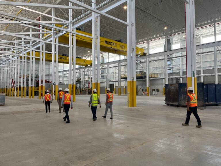 Broad interior view of a large high-bay industrial facility with roof steel